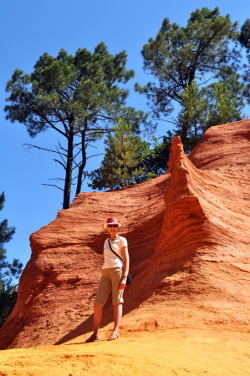 Susan Vreeland standing in front of a curved ochre wall in Le Sentier des Ocres